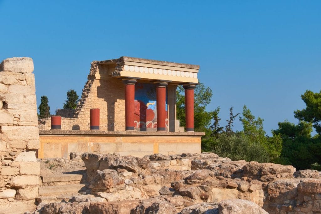 Ruins of Knossos Palace with restored red columns, stone walls, and a blue sky