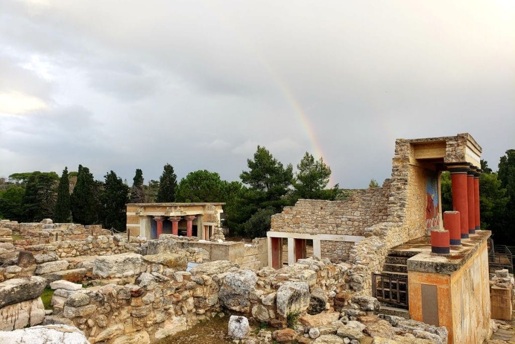 Knossos Palace ruins with restored red columns and a rainbow over the archaeological site