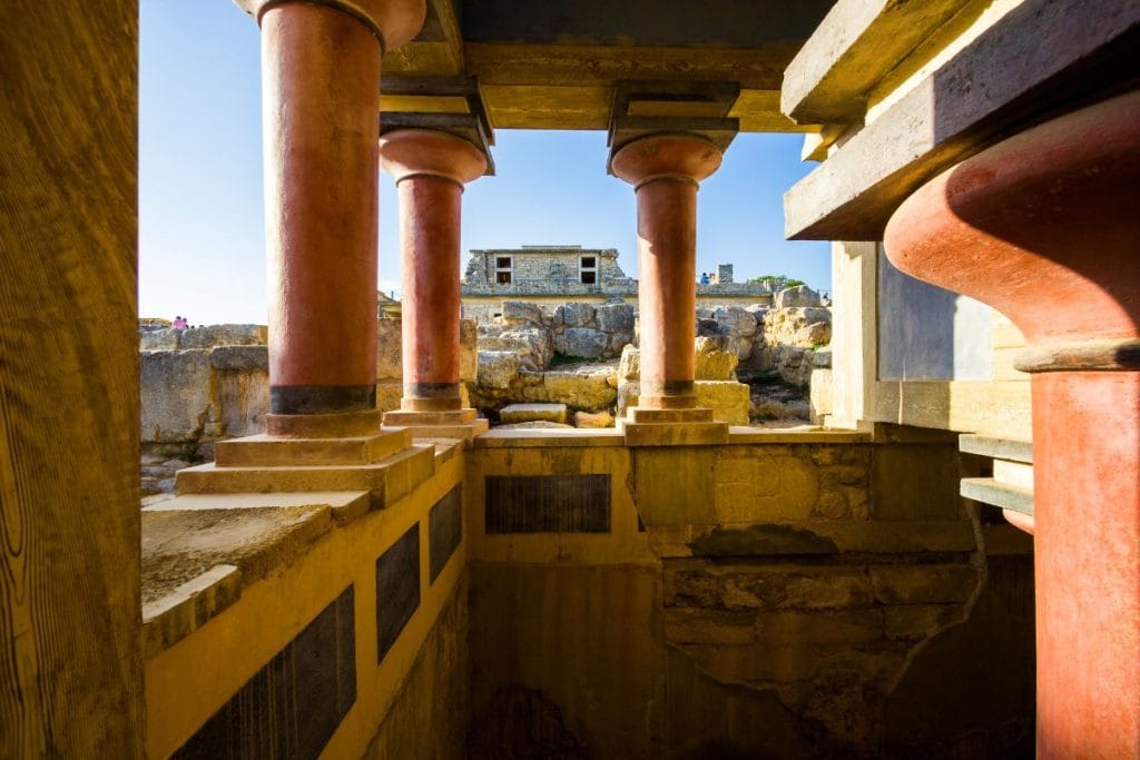 Interior view of restored red columns, stone walls, and palace ruins at Knossos